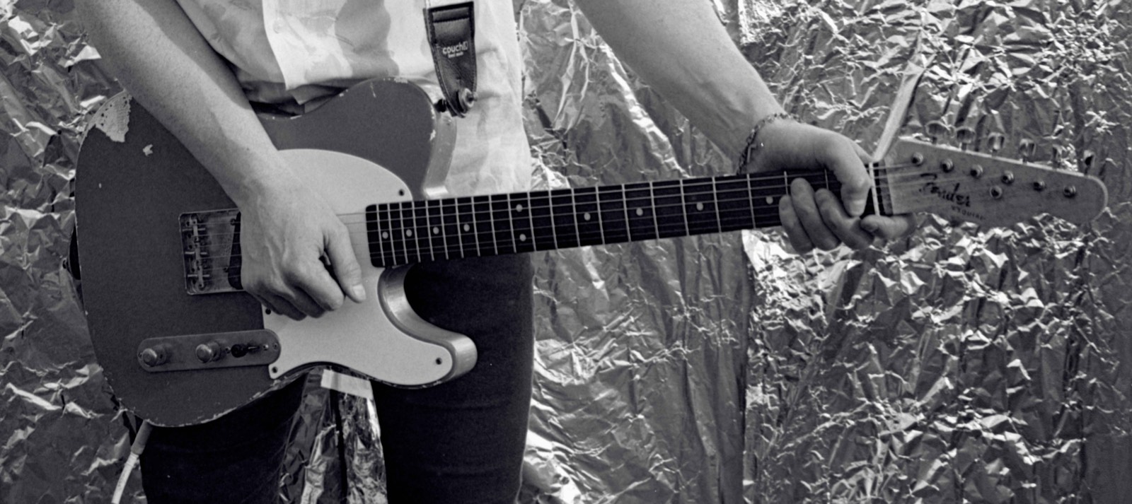 Black-and-white photo of a guitarist playing a Telecaster in front of crumpled foil